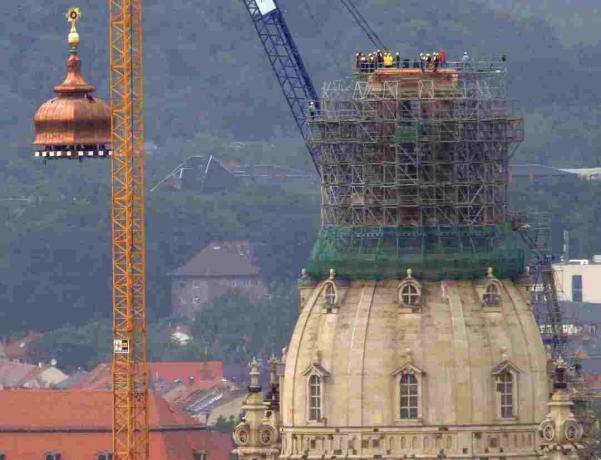 En kran løfter kobberkuppelen og det gyldne korset til toppen av den rekonstruerte Frauenkirche i Dresden, Tyskland