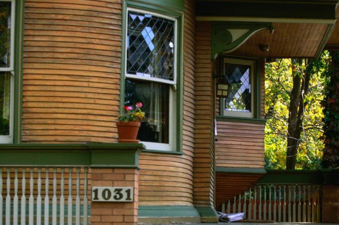 Detalj av veranda med avrundt hus, sidespor i naturlig tre med grønt dekor, dobbelthengte blyvinduer, dekorative korbler