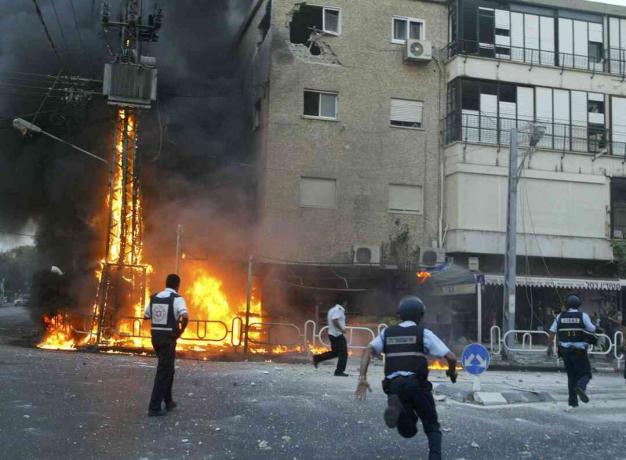 Israelske politimenn skynder seg til åstedet for en brennende elektrisitetspylon og skadet bygningsøyeblikk etter at en volley av Hizbollah-raketter slo til 13. juli 2006 i den nordlige byen Nahariya, Israel.