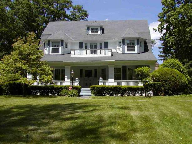Stort hvitt hus med enormt grå tak i front og stor, grønn gressplen