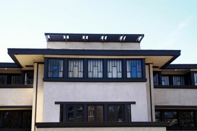 horisontalt orientert lyssidig hus med mørkebrunt dekor, flatt tak med enorme overheng og rader med vinduer med blyholdig glass