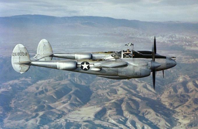 En sølv P-38 lynkjemper som flyr over fjell
