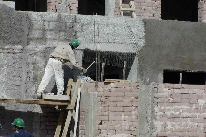 mann i hard hatt på stillaser som jobber på jordklossveggen