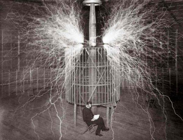 Nikola Tesla sitter i laboratoriet i Colorado Springs ved siden av det enorme 