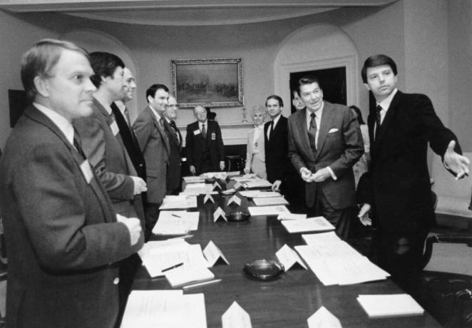Et svart -hvitt bilde av Ronald Reagan og flere andre menn i dresser rundt et langt konferansebord