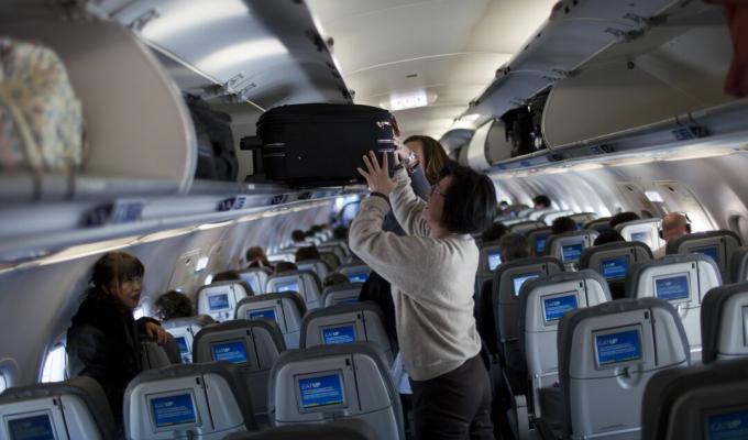 Mujer colocando maleta en compartmento superior de avión.