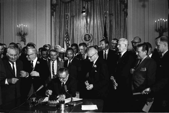 President Lyndon B. Johnson signerer 1964 Civil Rights Act som Martin Luther King, Jr., og andre, ser på.